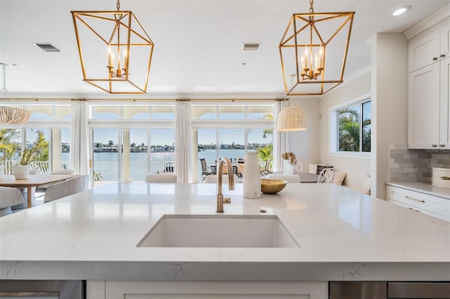 kitchen with visible vents, an inviting chandelier, an island with sink, a sink, and backsplash