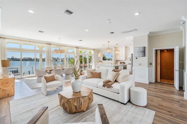 living area with light wood-type flooring, visible vents, a water view, and crown molding