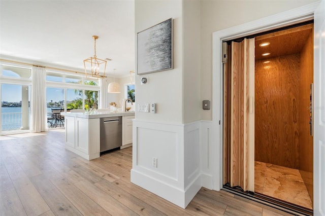 kitchen with light wood-style flooring, elevator, dishwasher, and white cabinets