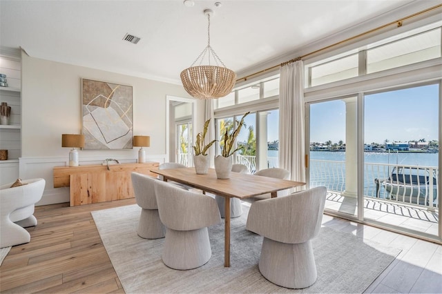 dining space featuring a wainscoted wall, visible vents, an inviting chandelier, light wood-style floors, and a water view