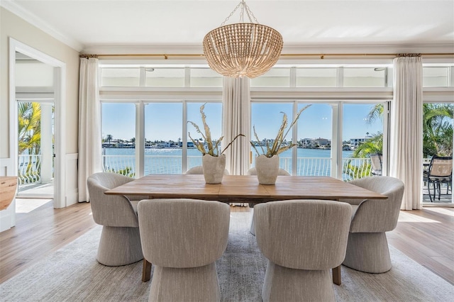 dining area with a wealth of natural light, a water view, an inviting chandelier, and ornamental molding