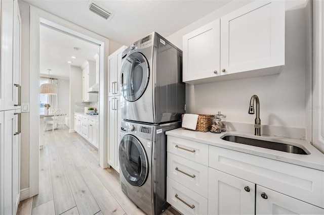 washroom with visible vents, a sink, cabinet space, light wood-style floors, and stacked washer / dryer