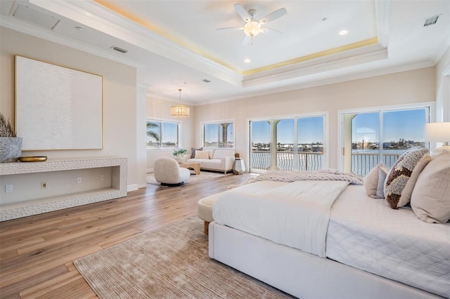 bedroom featuring visible vents, wood finished floors, a tray ceiling, and access to outside