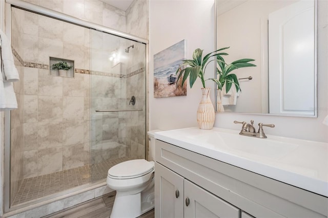 bathroom with a stall shower, toilet, vanity, and wood finished floors