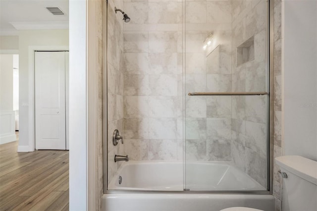 bathroom featuring enclosed tub / shower combo, toilet, wood finished floors, and crown molding