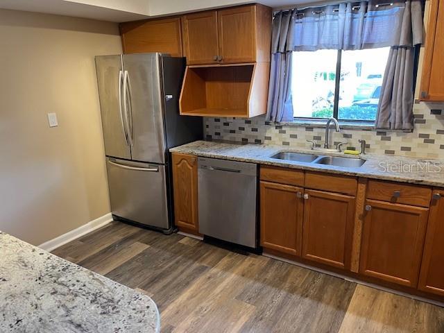 kitchen featuring dark wood-style flooring, a sink, appliances with stainless steel finishes, brown cabinets, and backsplash