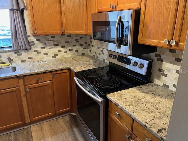 kitchen with light stone counters, stainless steel appliances, brown cabinets, and dark wood finished floors