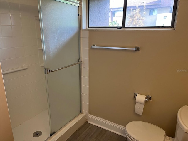 full bath with toilet, wood finished floors, a stall shower, and baseboards