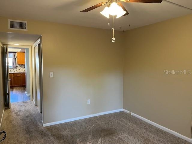 carpeted empty room with baseboards, visible vents, and ceiling fan