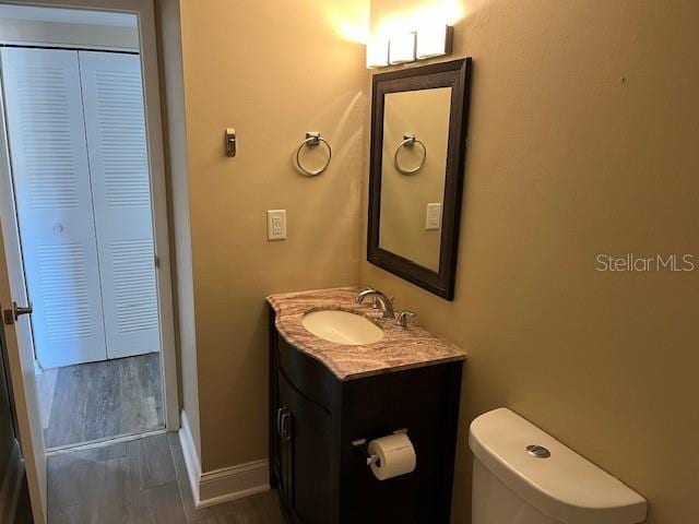 bathroom with vanity, wood finished floors, baseboards, a closet, and toilet