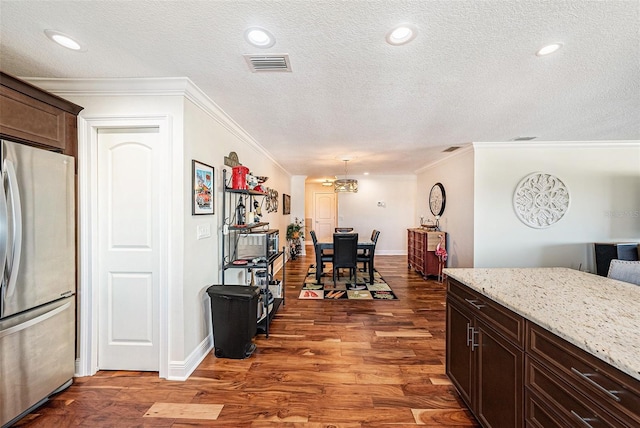 kitchen featuring visible vents, light stone countertops, dark brown cabinetry, freestanding refrigerator, and dark wood-style flooring