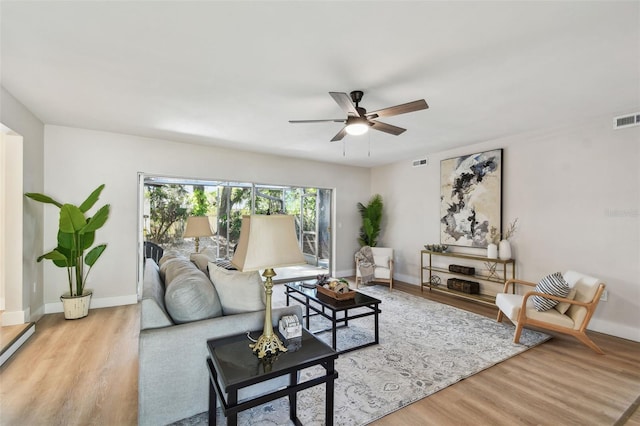 living room featuring ceiling fan, visible vents, light wood-type flooring, and baseboards