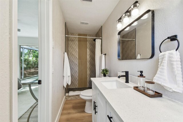 bathroom with visible vents, toilet, wood finished floors, a tile shower, and vanity