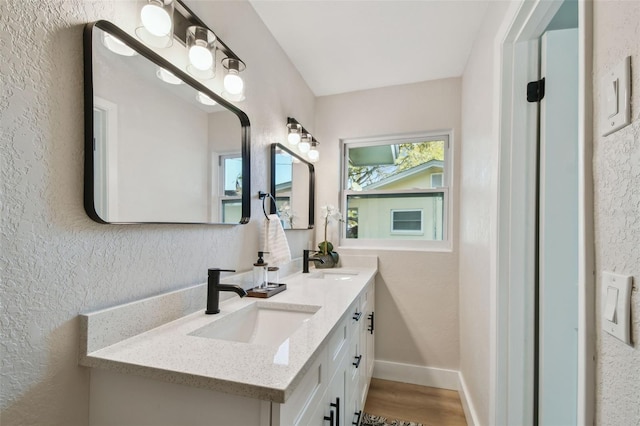 bathroom with a sink, baseboards, double vanity, and a textured wall