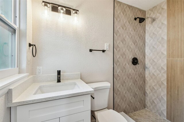 full bathroom with vanity, toilet, a textured wall, and a tile shower