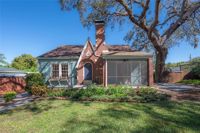 tudor-style house with a front yard, fence, a sunroom, a chimney, and brick siding