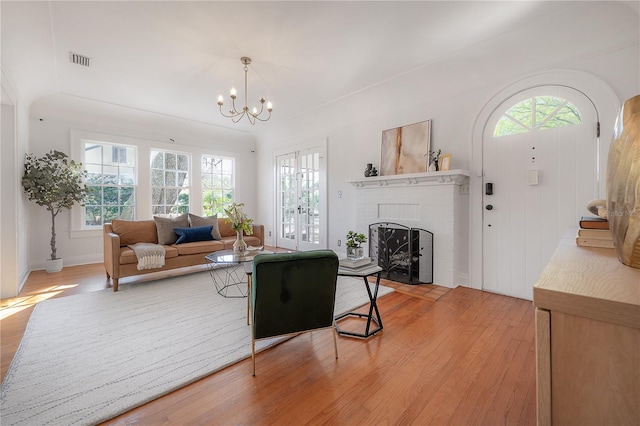 living area with visible vents, a brick fireplace, a chandelier, and light wood finished floors