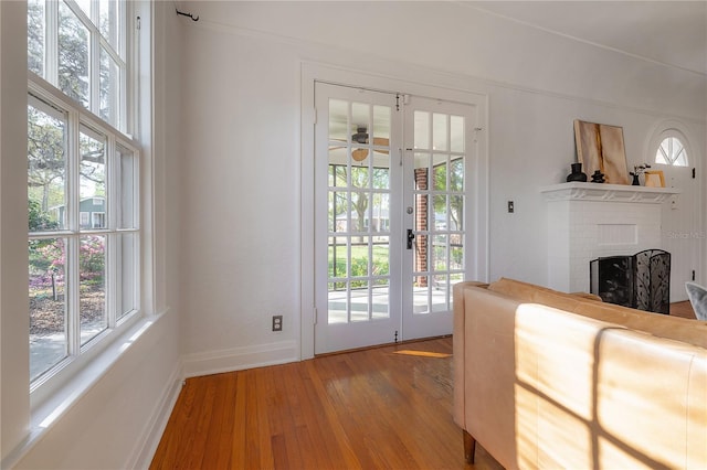 doorway to outside with light wood finished floors, a brick fireplace, baseboards, ceiling fan, and french doors