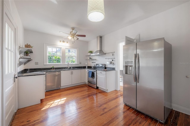 kitchen featuring dark countertops, stainless steel appliances, wall chimney range hood, and open shelves