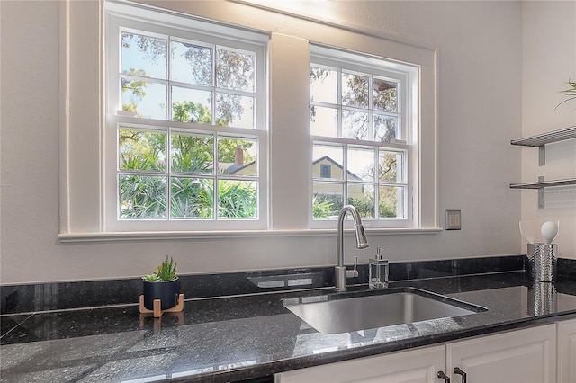 kitchen featuring white cabinetry, open shelves, dark stone countertops, and a sink