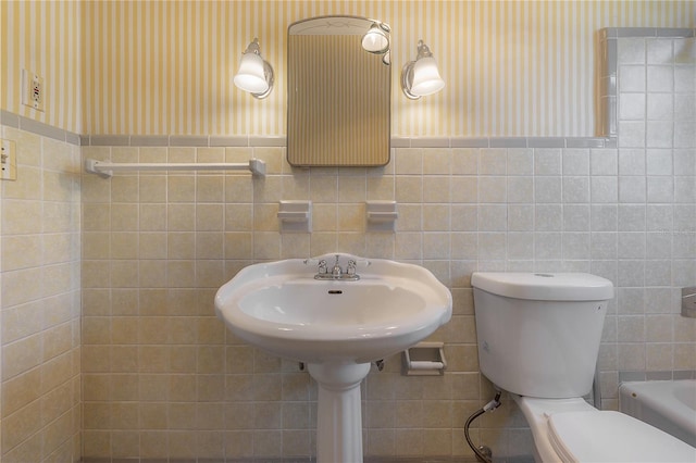 full bathroom featuring a washtub, toilet, wainscoting, and wallpapered walls