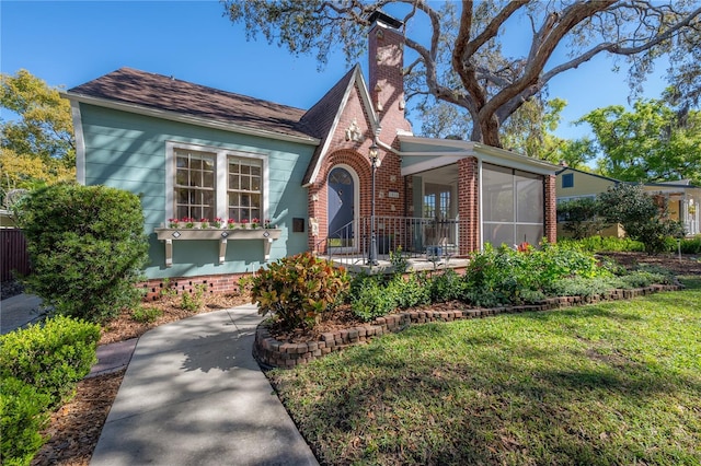 english style home with brick siding, a chimney, a front yard, and a sunroom