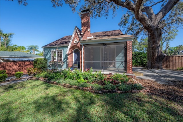 view of front facade featuring fence, a sunroom, a chimney, a front lawn, and brick siding