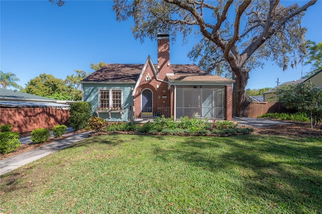 view of front of house featuring fence, a front yard, a sunroom, brick siding, and a chimney