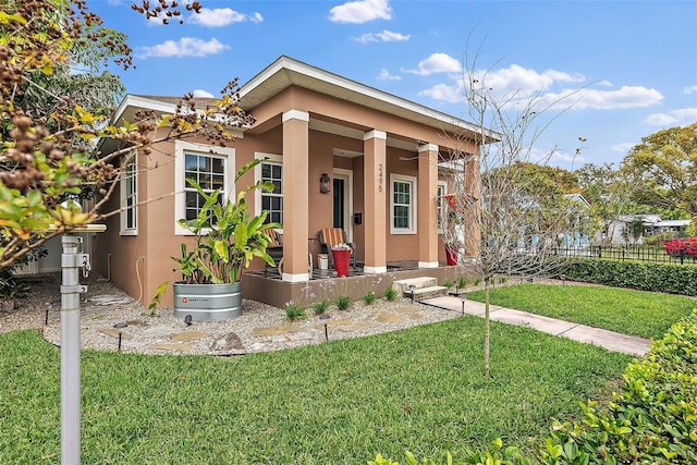 view of front of house with stucco siding, a porch, a front lawn, and fence