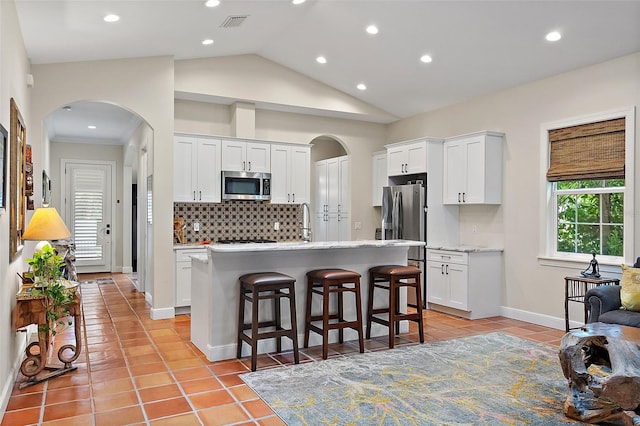 kitchen with light tile patterned flooring, arched walkways, stainless steel appliances, decorative backsplash, and white cabinetry