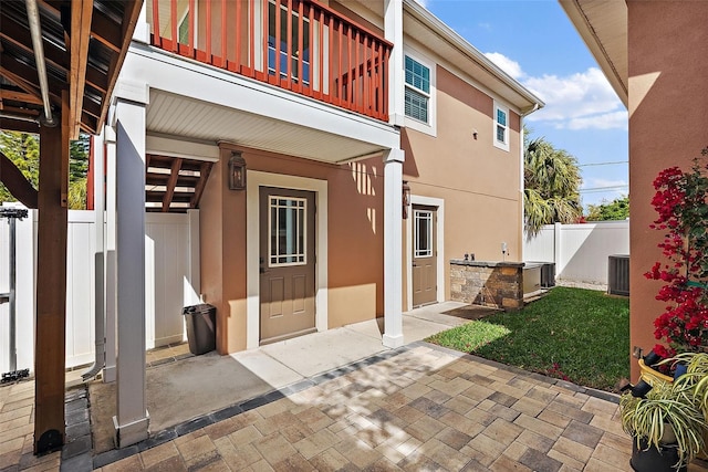 entrance to property featuring stucco siding, central air condition unit, a balcony, and fence