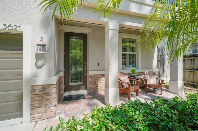 property entrance featuring stone siding, covered porch, and stucco siding