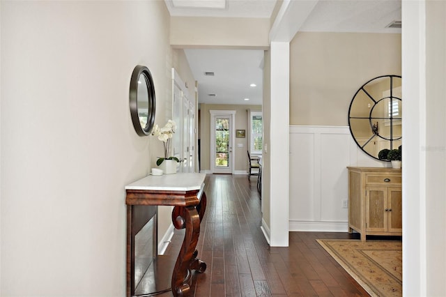 hall with a decorative wall, dark wood-type flooring, visible vents, and a wainscoted wall