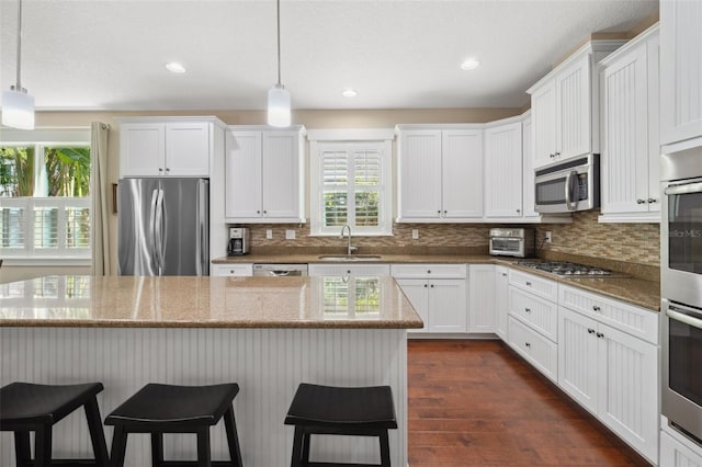 kitchen with a kitchen breakfast bar, stainless steel appliances, dark wood-style floors, white cabinetry, and a sink