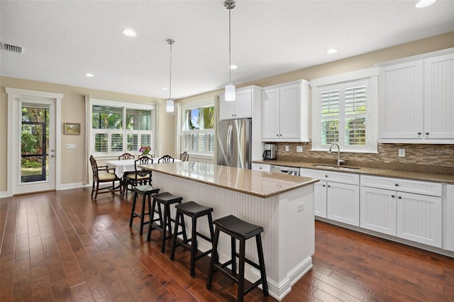 kitchen with stainless steel refrigerator, a sink, a center island, a breakfast bar area, and dark wood-style flooring