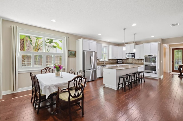 dining space with baseboards, visible vents, dark wood-style flooring, and a textured ceiling