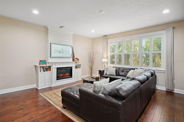 living area featuring dark wood-style floors, visible vents, baseboards, and a glass covered fireplace