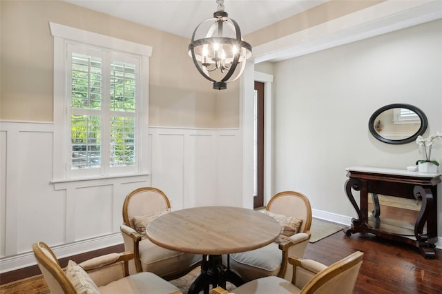 dining area with dark wood-style floors, a chandelier, wainscoting, and a decorative wall