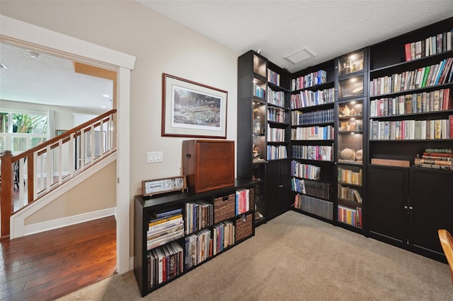 living area with a textured ceiling, carpet, stairs, and bookshelves