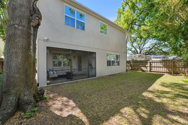 rear view of property featuring stucco siding, a sunroom, a yard, and fence