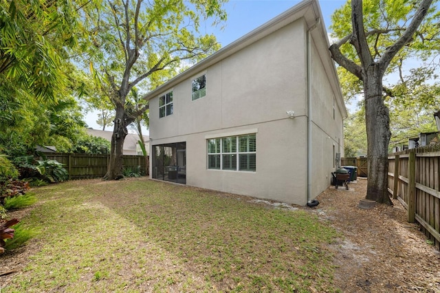 back of property featuring stucco siding, a lawn, a fenced backyard, and a sunroom