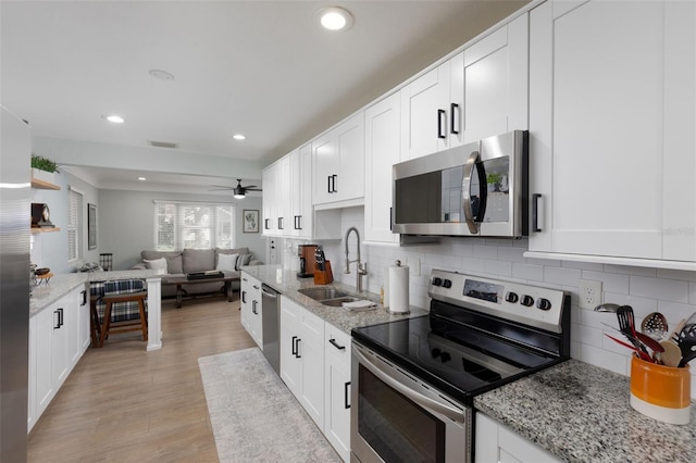 kitchen with light wood-style flooring, a sink, appliances with stainless steel finishes, white cabinetry, and open floor plan