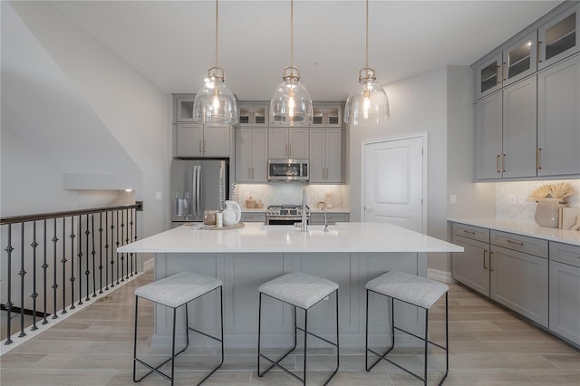 kitchen featuring wood finish floors, gray cabinetry, an island with sink, a kitchen breakfast bar, and appliances with stainless steel finishes