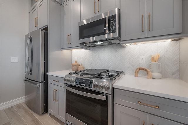 kitchen with light wood-type flooring, gray cabinets, backsplash, stainless steel appliances, and light countertops