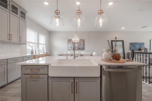 kitchen featuring tasteful backsplash, light countertops, gray cabinets, stainless steel dishwasher, and a sink