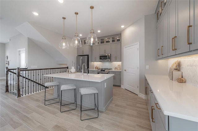 kitchen with wood finish floors, gray cabinetry, appliances with stainless steel finishes, a kitchen bar, and backsplash