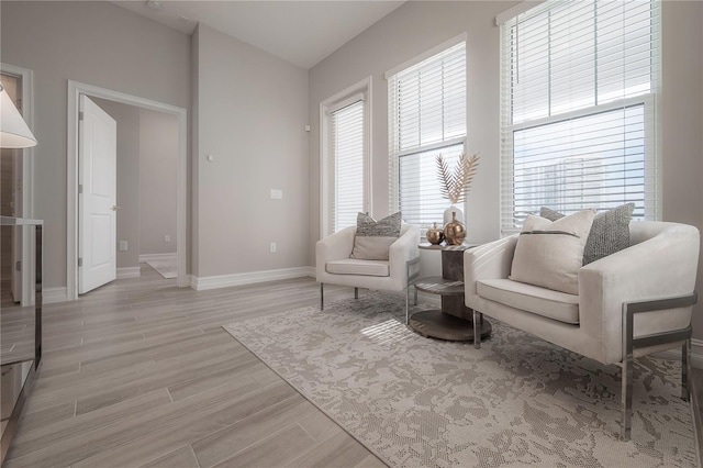 living area featuring light wood finished floors, lofted ceiling, and baseboards