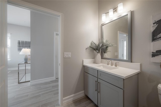 bathroom with wood finish floors, baseboards, toilet, and vanity