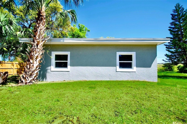 view of side of property with stucco siding, a lawn, and fence