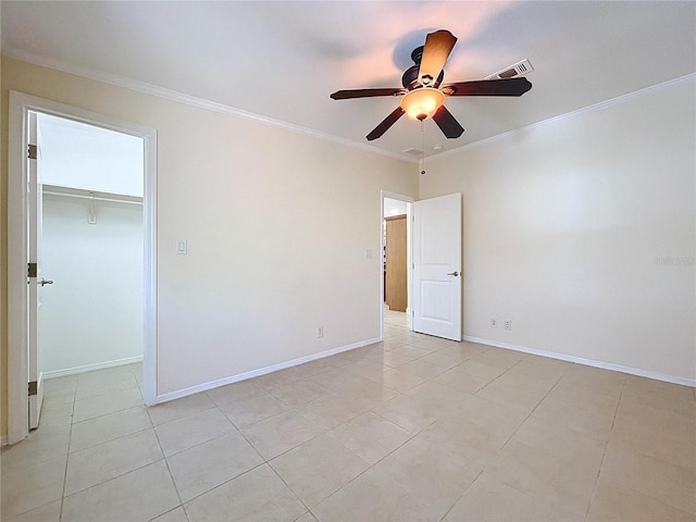 unfurnished bedroom with light tile patterned floors, baseboards, ceiling fan, ornamental molding, and a walk in closet